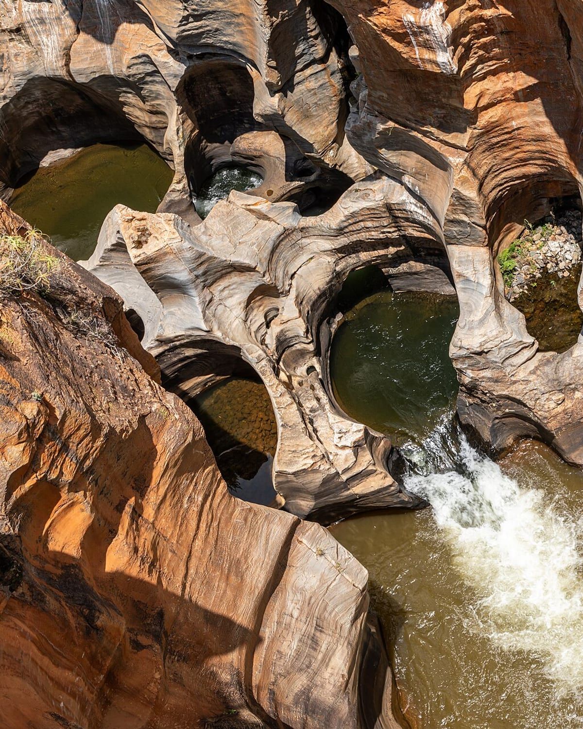 Bourke's Luck Potholes — cylindrical hollows carved into pale rock by the river, with water running between them. Photo by Dietmar Rabich, CC BY-SA 4.0